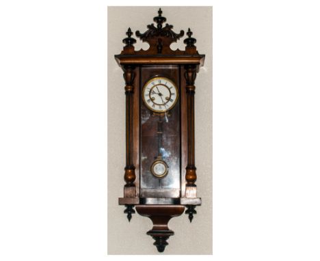 A German Vienna Style Wall Clock, in a walnut case. With a scroll top with finials and ebonised decoration. With white enamel
