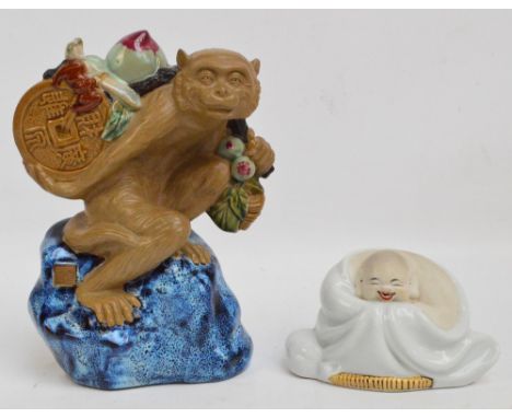 A 20th century Chinese ceramic figure of a monkey seated on a rock, carrying a large token, a peach, a button hook and a bat 