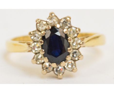 An 18ct yellow gold dress ring set with a central oval sapphire surrounded by twelve diamonds, on a pierced gallery, size M/N