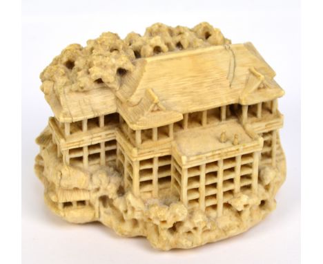 A detailed Japanese carved ivory netsuke modelled as a multi-storied dwelling with steps to one side, a pagoda to the reverse