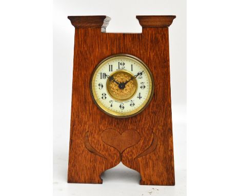 An oak Arts and Crafts mantel clock, the angled case set with central heart shaped motif beneath a circular dial set with Ara