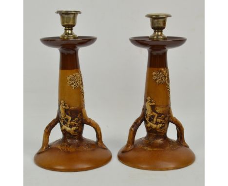 A pair of Royal Doulton Lambeth candlesticks with embossed fox hunting scenes, foliate handles and circular bases, with hallm
