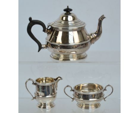 A George V hallmarked silver three piece tea service comprising a teapot of squat baluster form with loop handle and leaf cap