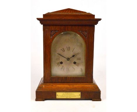 An early 20th century oak cased mantel clock, with arched silvered dial set with Roman numerals and bearing presentation plaq
