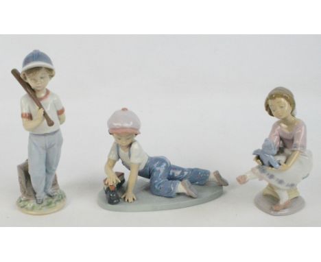 Three Lladro figures; a boy playing with a train, a boy holding a baseball bat and a seated girl playing with a teddy bear (3