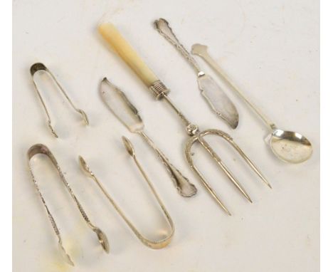 A small group of silver items including three pairs of sugar tongs, a pair of butter knives and a spoon, also a plated bread 