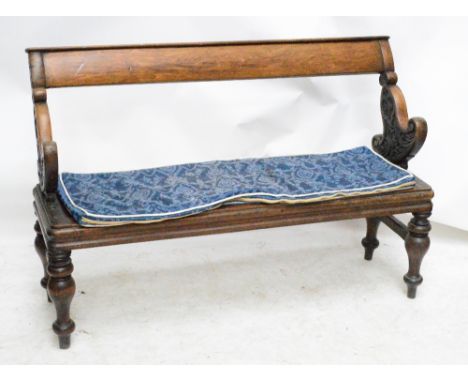 A Victorian mahogany bench with fixed top rail and twin carved pivoting end supports allowing people to sit facing either dir