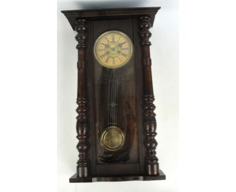 A large eight day spring driven wall clock, the circular enamel dial set with Roman numerals, flanked with ring turned column