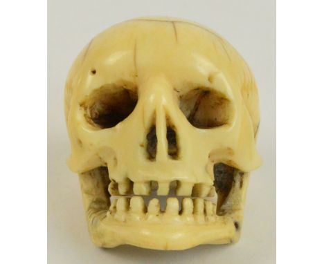 A Japanese Meiji period carved ivory netsuke modelled as a human skull with cranial detail and pinned jaw, height 3.5cm. COND