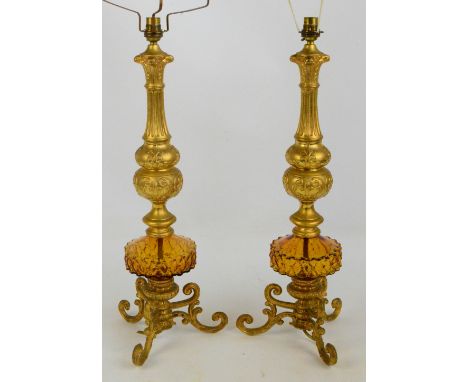 A pair of decorative gilt metal and amber glass table lamps with fluted and knopped stems, on scroll decorated tripod base, h