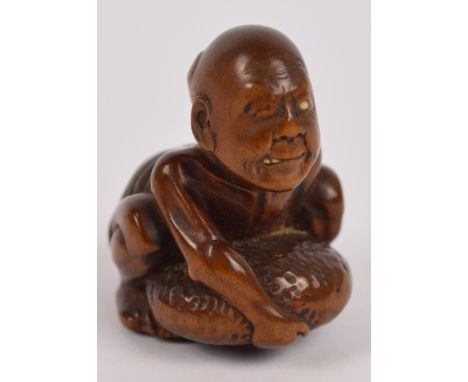A Japanese Meiji period carved boxwood netsuke modelled as a man embracing a pebble, with ivory inset eye and teeth and a rec