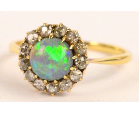 A yellow metal diamond and opal ring, the central oval cabochon set within a border of thirteen old cut diamonds, opal diamet