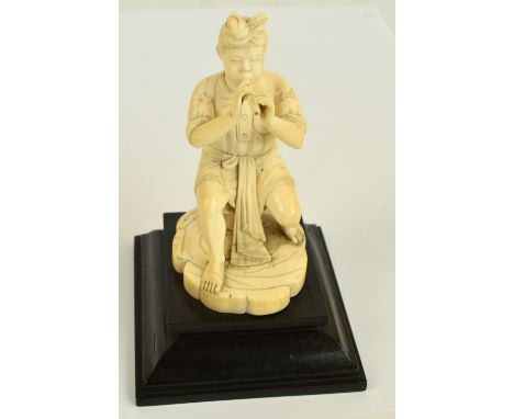 A Japanese Meiji period carved ivory figure of a seated man playing a flute, on lobed oval base and rectangular stepped pedes