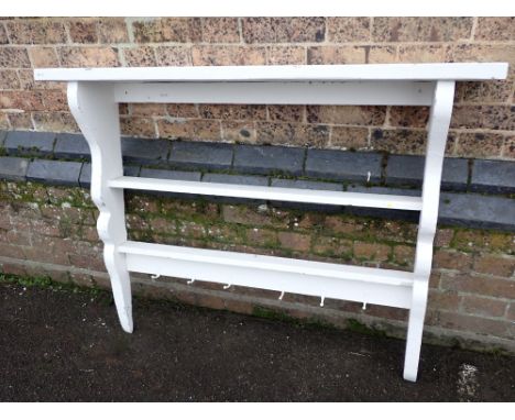 A PAINTED KITCHEN WALL RACKthree shelves with shaped sides and hooks under, the top shelf 122cm wide
