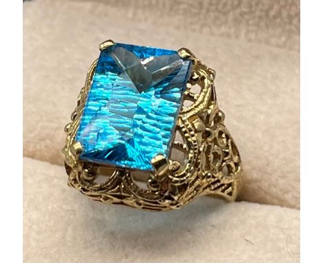 9ct yellow gold ornate ring set with an Emerald cut Blue Topaz stone. [Ring size N] [6.79Grams] 