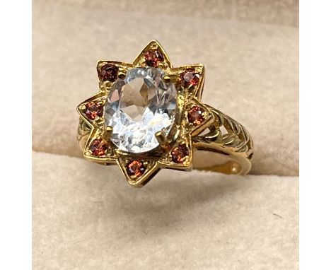 9ct yellow gold ring set with a cushion cut aquamarine stone surrounded by round cut red garnet stones. [Ring size N] [4Grams