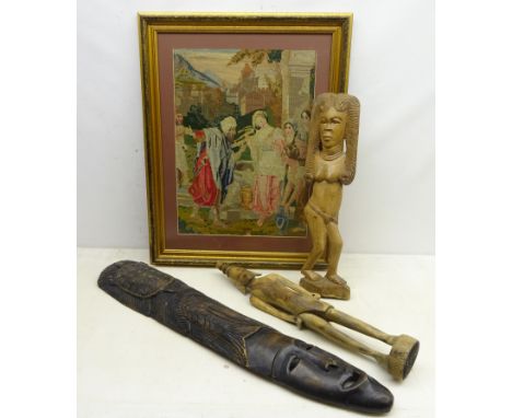 Two Tribal art carved figures and a carved tribal elongated mask, H89cm and woolwork tapestry picture of figures in a village