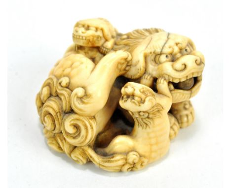 A good Japanese Meiji period carved ivory netsuke modelled as a chichi with rolling ball in its mouth and two pups by its sid