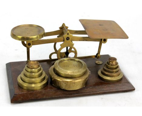 A pair of early 20th century brass postal scales with associated weights and on oak plinth, 21cm.