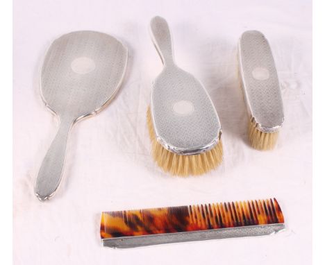 A silver backed hand mirror with engine turned decoration, two matching brushes and a comb