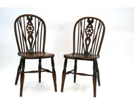 A pair of elm seated stick and wheelback dining chairs, raised on turned tapering front supports united by H stretchers 