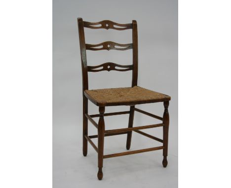 A set of four elm pierced ladder back dining chairs, with rush work seats, raised on turned baluster supports united by spind