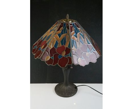 Tiffany style table lamp, with stained glass shade in red, salmon pink and blue, above a metal lamp base with cast foliate de