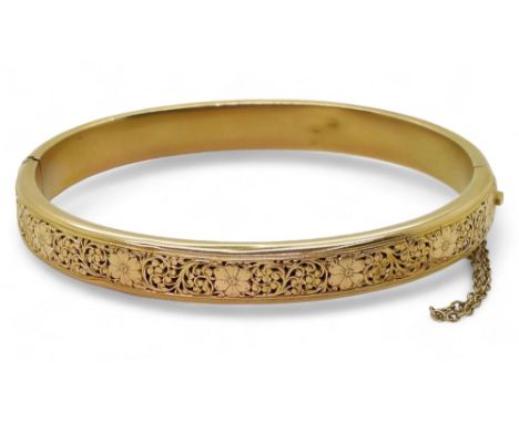 A FLORAL BANGLE the front with pierced panel of flowers and foliage, made in 'bloomed' bright yellow metal, with box clasp. i