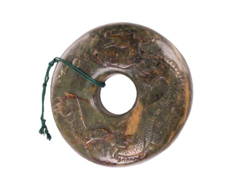 A Chinese carved moss variegated jade Bi disk form carving, Qing Dynasty, probably Tongzhi, the face carved with a rampaging 
