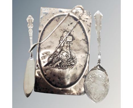 A silver emobssed panel together with a further silver pair of sugar tongs caddy spoon and butter knife. 