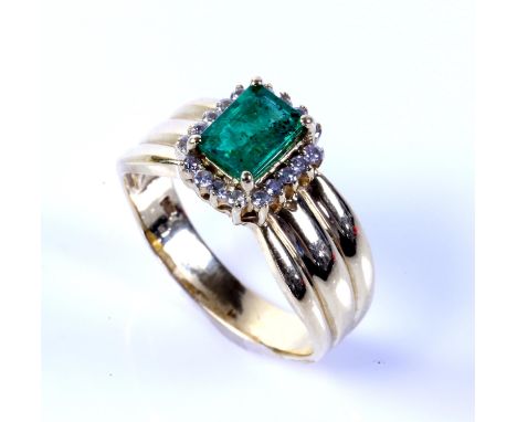 Emerald and diamond ring, central emerald cut emerald, with a surround of round brilliant cut diamonds, mounted on a wide rid