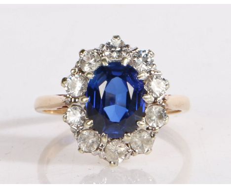 9 carat gold ring set with a central oval blue paste stone and surrounded by a band of clear paste, ring size M, 3.5g