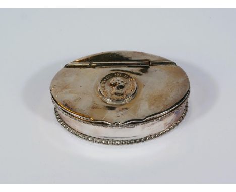 A 19th century oval white metal snuff box with 1806 coin top, hinged lid and piecrust border 