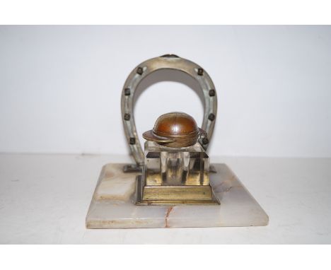An Edwardian desk ink stand the original glass inkwell with a jockey cap hinged lid and horseshoe shaped pen rest on a white 