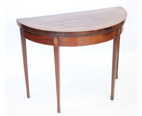 A George III demi-lune mahogany card table in the Sheraton manner, the rosewood cross banded top opening to a baize lined gam