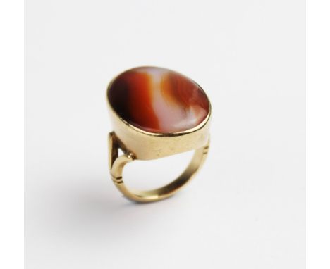 A carnelian set 9ct gold dress ring, the central polished carnelian cabochon measuring 24mm x 18mm, bezel set to a plain poli