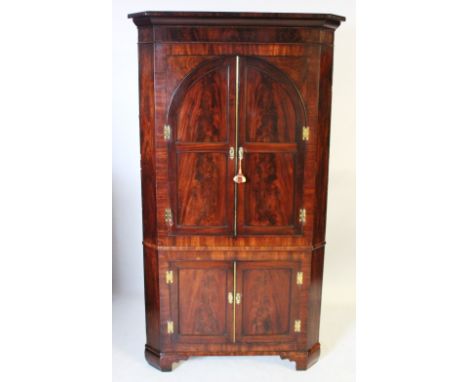 A George III mahogany free standing corner cupboard, the cavetto cornice above a pair of cupboard doors applied with arched m