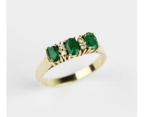 An emerald and diamond ring, comprising three mixed cut oval emeralds each measuring 4.7mm x 3mm, interspersed with four smal