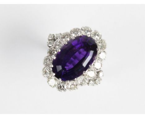 An amethyst and diamond cocktail ring, the central oval step cut amethyst (measuring 15.5mm x 10mm x 7.5mm), claw set to a cl