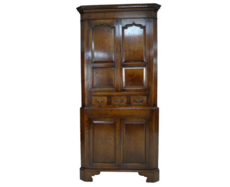 An oak corner cupboard in 18th century Welsh style, late 20th century, of two sections with twin shaped doors over three smal