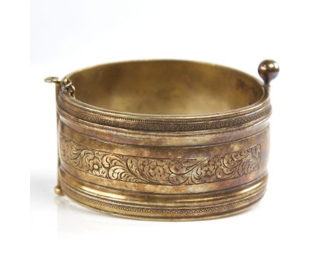 A 19th century unmarked silver? gilt hinged bangle, engraved floral panels, band width 32.7mm, internal diameter 59mm, 61.5gG