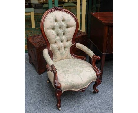 A Victorian carved walnut armchair with button back, on scroll supports and with pot casters