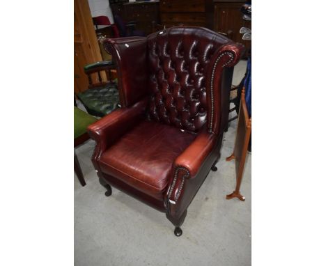 A modern oxblood leather wingback armchair having button back
