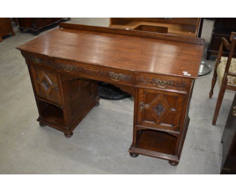 An early 20th Century oak desk, having Jacobean style cushioned panel doors and shaped carved drawers, label to drawer for R.