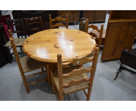 A vintage yellow pine circular kitchen table and set of four similar ladder back chairs with woven seats, table diameter appr