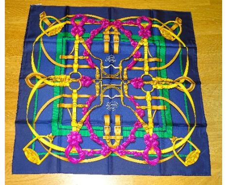 A silk Hermes scarf, decorated with gold horse bits, bridles and stirrups on navy blue ground with green and pink ribbons, in