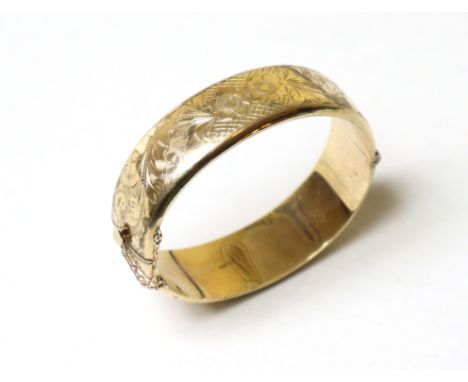 A 9ct gold stiff-hinged bangle with engraved floral decoration to one half, with safety chain (22.2g).