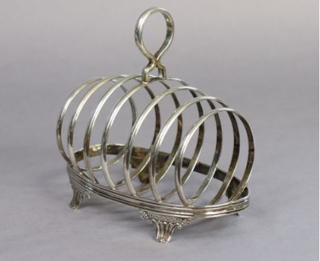 A late Victorian silver large toast rack of six oval divisions, with centre ring handle &amp; on four neo-classical fluted fe