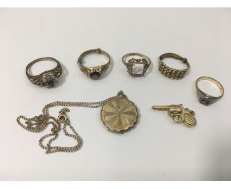 A collection of gold items comprising rings, a locket and a trinket in the form of a gun.