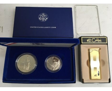 A boxed set of two 1986  United States Liberty silver coins and a cased Gold tone Calibri lighter.